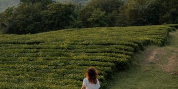 A Woman in White Shirt Walking on Green Grass Field